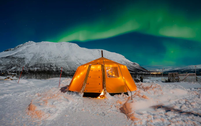 Tent under Northern Lights in snowy Tromso Lapland landscape.