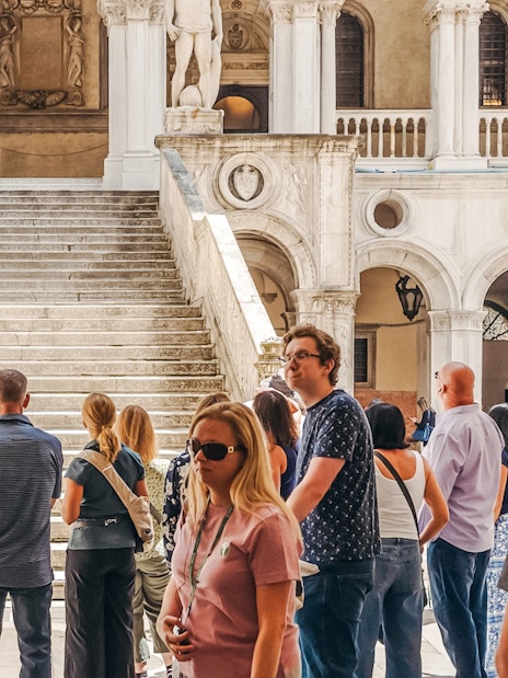 Tour group near Giants' Staircase at Doge's Palace, Venice, with guide explaining architecture.