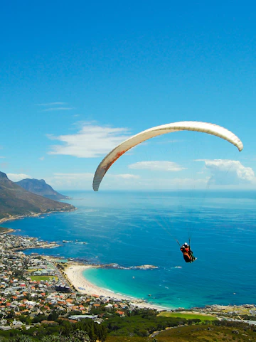 Paraglider soaring over Cape Town coastline, South Africa, with ocean and mountains in view.