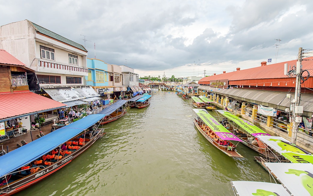 Boats lined up at Amphawa Floating Market, Thailand, with colorful awnings and riverside shops.