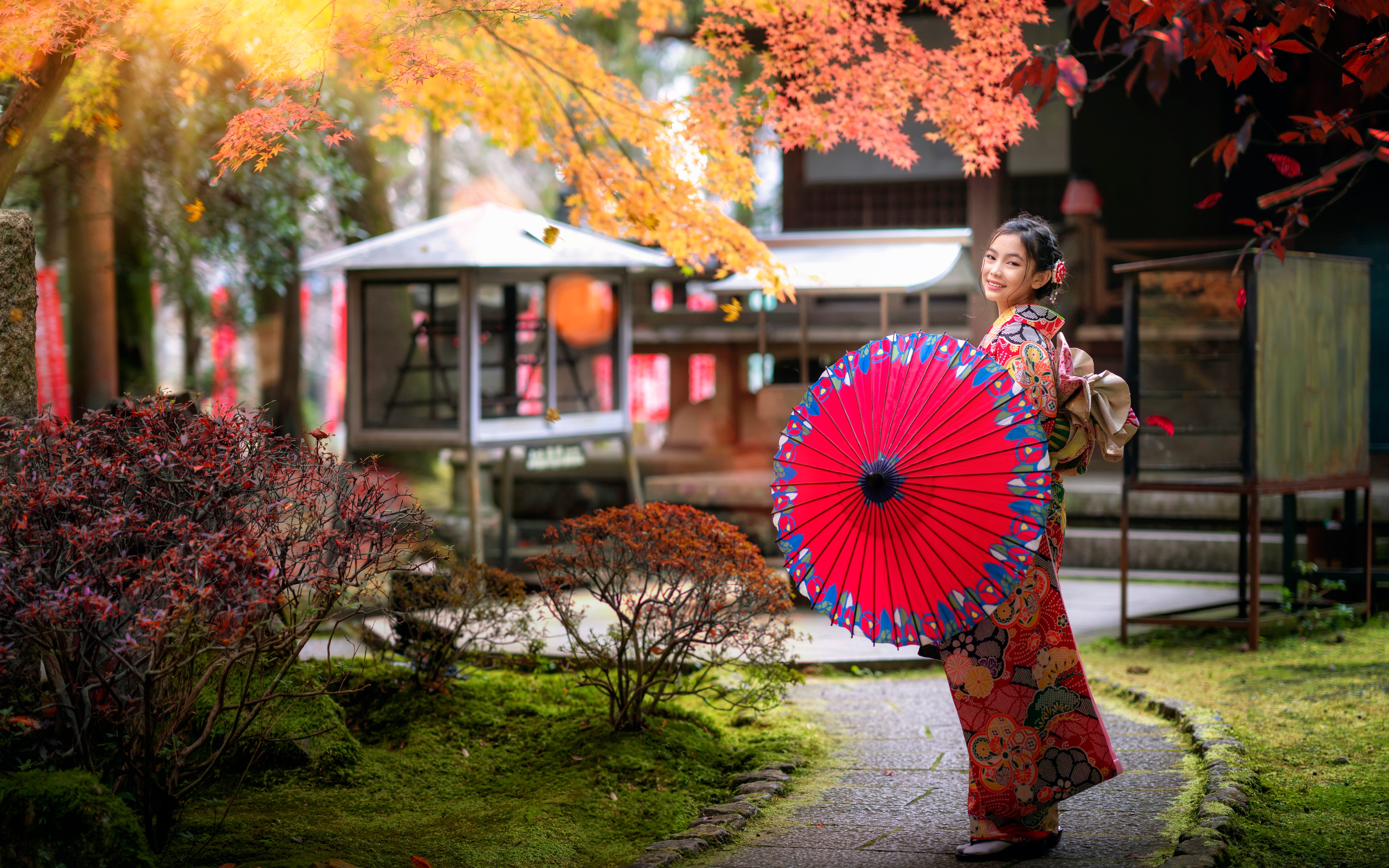 Japanese woman in kimono with red umbrella walking in temple garden.