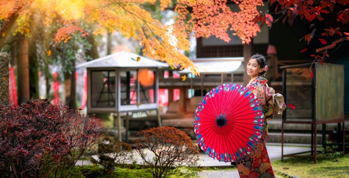 Japanese woman in kimono with red umbrella walking in temple garden.