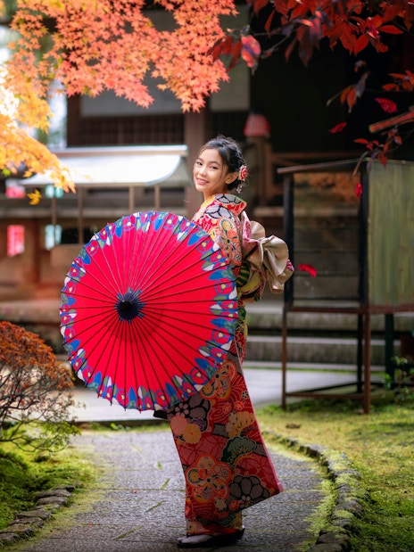 Japanese woman in kimono with red umbrella walking in temple garden.
