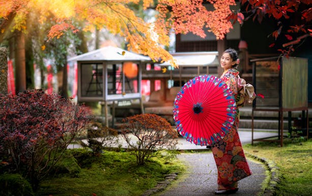 Japanese woman in kimono with red umbrella walking in temple garden.