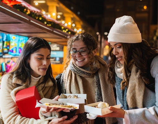 Friends enjoying desserts at a Christmas market food stall at night.