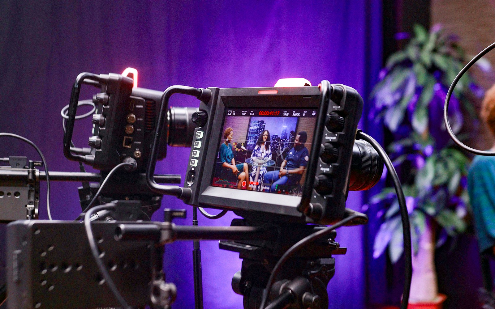 Camcorder setup capturing a television broadcast with three people in discussion.