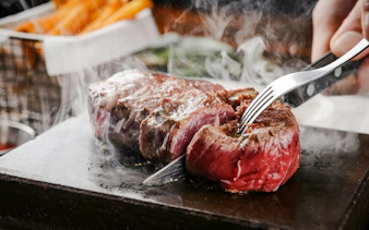 Cutting a steak on a steaming hot stone with a fork and knife.