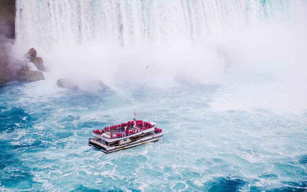 Tourist boat near the base of Niagara Falls surrounded by mist and churning water.
