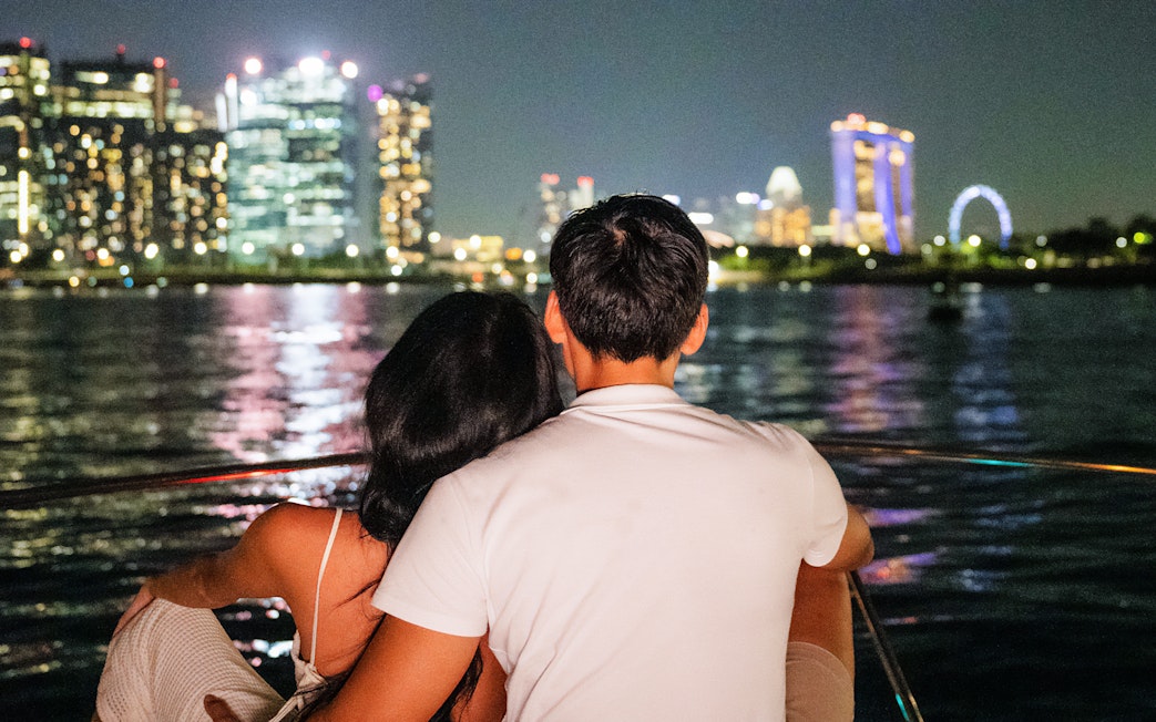 Couple on yacht enjoying Marina Bay Sands skyline at night.