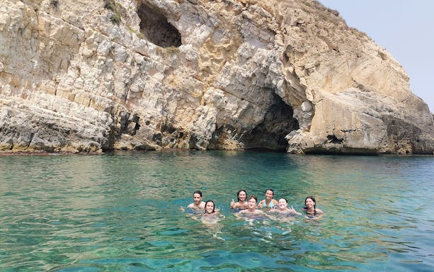 Group swimming near sea caves on Ortigia Island sightseeing cruise.