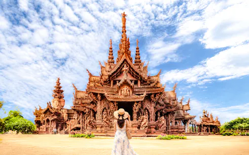 Sanctuary of Truth in Pattaya with visitor in foreground, clear sky above.