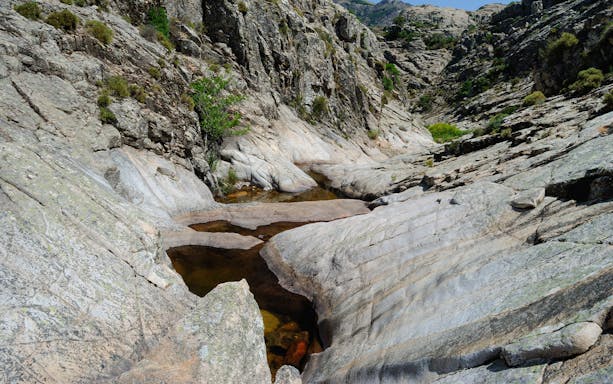 Trekker crossing rocky terrain towards Piscina Irgas Waterfall in Villacidro, Cagliari.