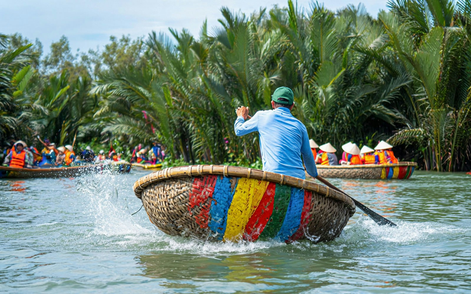 Guide rowing a colorful basket boat on Hoi An river with tourists in the background.