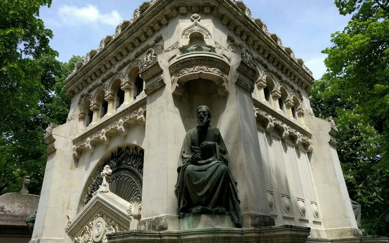 Ornate mausoleum with statue at Bellu Cemetery, Bucharest, surrounded by trees.