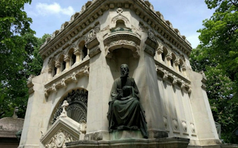 Ornate mausoleum with statue at Bellu Cemetery, Bucharest, surrounded by trees.