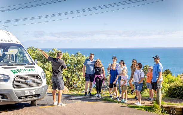 Group gathered near shuttle for Waiheke Island zipline adventure with ocean view.