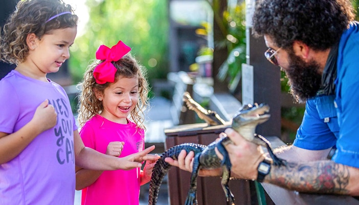 Children interacting with a small alligator at Everglades reptile exhibit.
