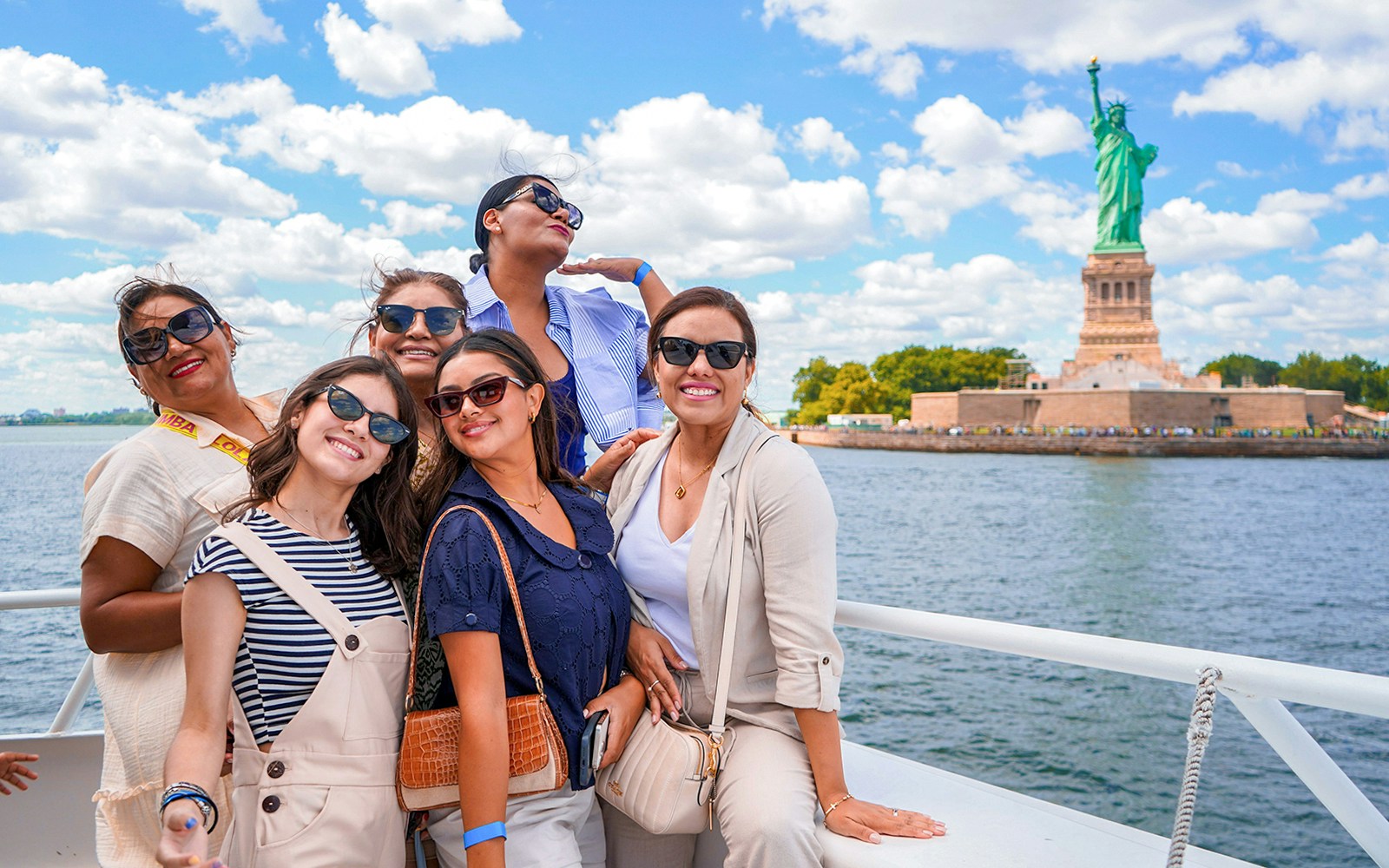 Sightseeing cruise passengers with Statue of Liberty and New York City skyline in background.
