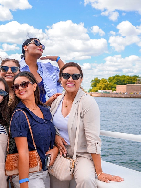 Sightseeing cruise passengers with Statue of Liberty and New York City skyline in background.
