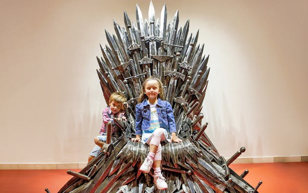 Children sitting on a steel throne at Gallery of Steel Figures, Prague.