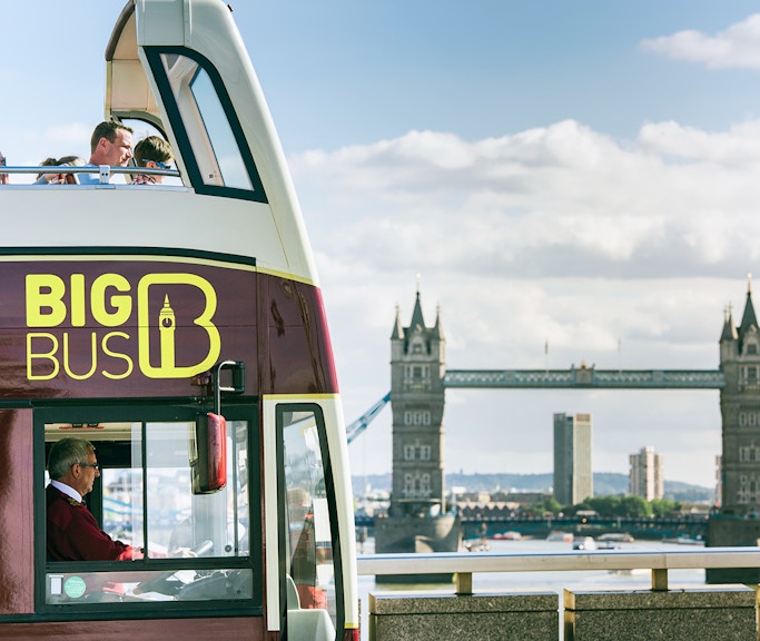 Open-top Big Bus London tour passing by Tower Bridge.
