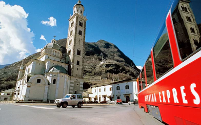 Bernina Express train passing by a historic church in Tirano, Italy.