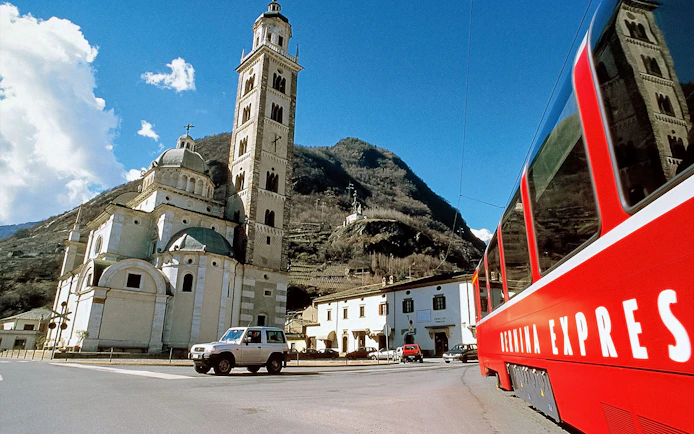 Bernina Express train passing by a historic church in Tirano, Italy.