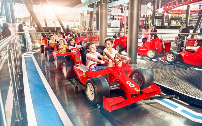Children enjoying a ride in red race cars at a YAS Island theme park, Abu Dhabi.