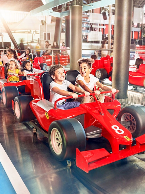 Children enjoying a ride in red race cars at a YAS Island theme park, Abu Dhabi.