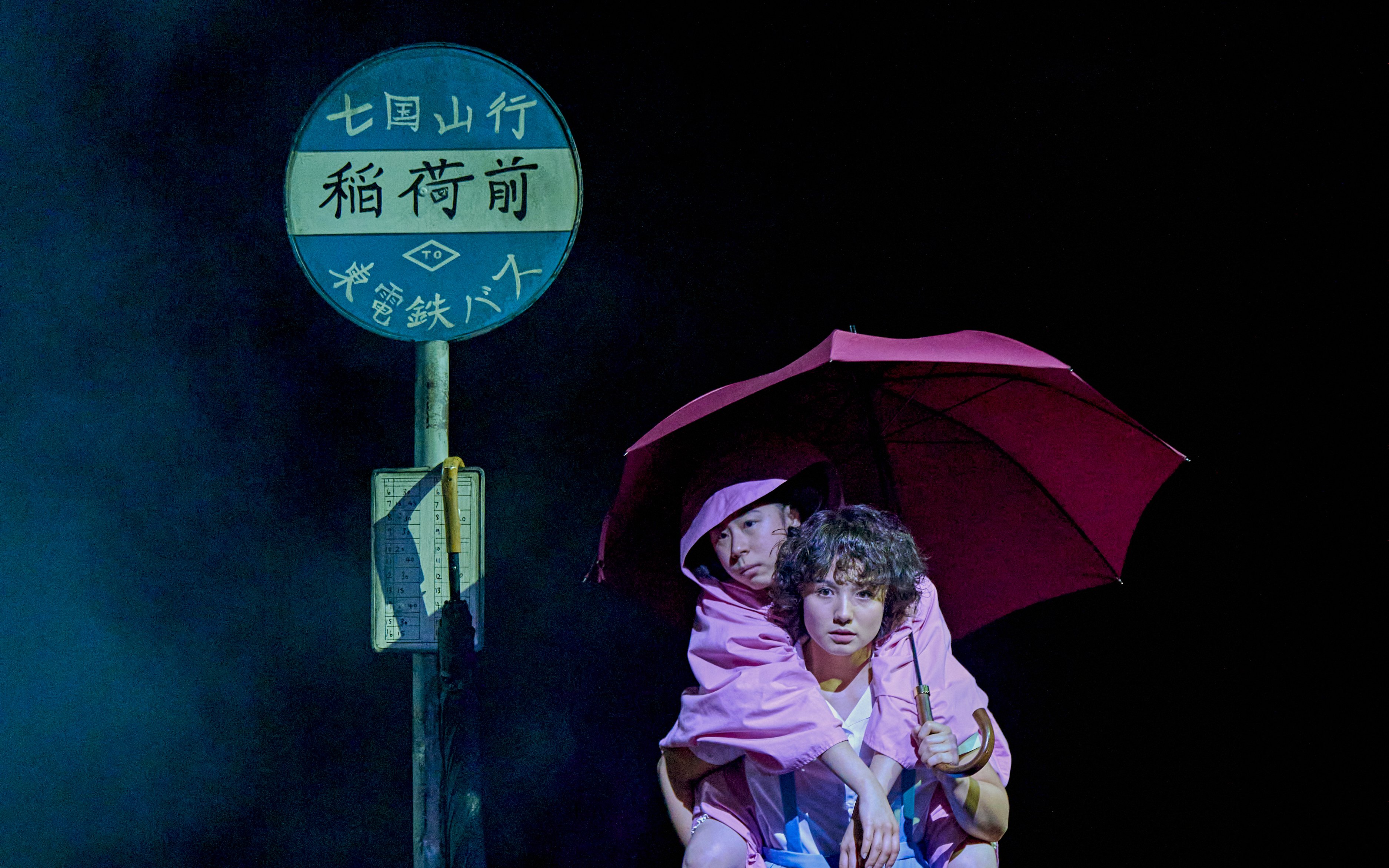 Two people in pink raincoats under an umbrella at a bus stop, My Neighbour Totoro production.