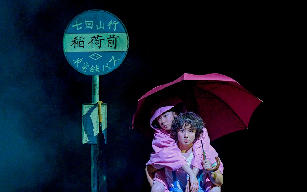 Two people in pink raincoats under an umbrella at a bus stop, My Neighbour Totoro production.