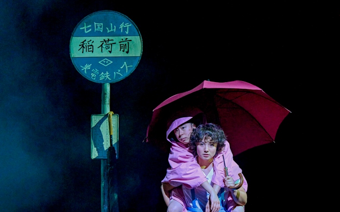 Two people in pink raincoats under an umbrella at a bus stop, My Neighbour Totoro production.