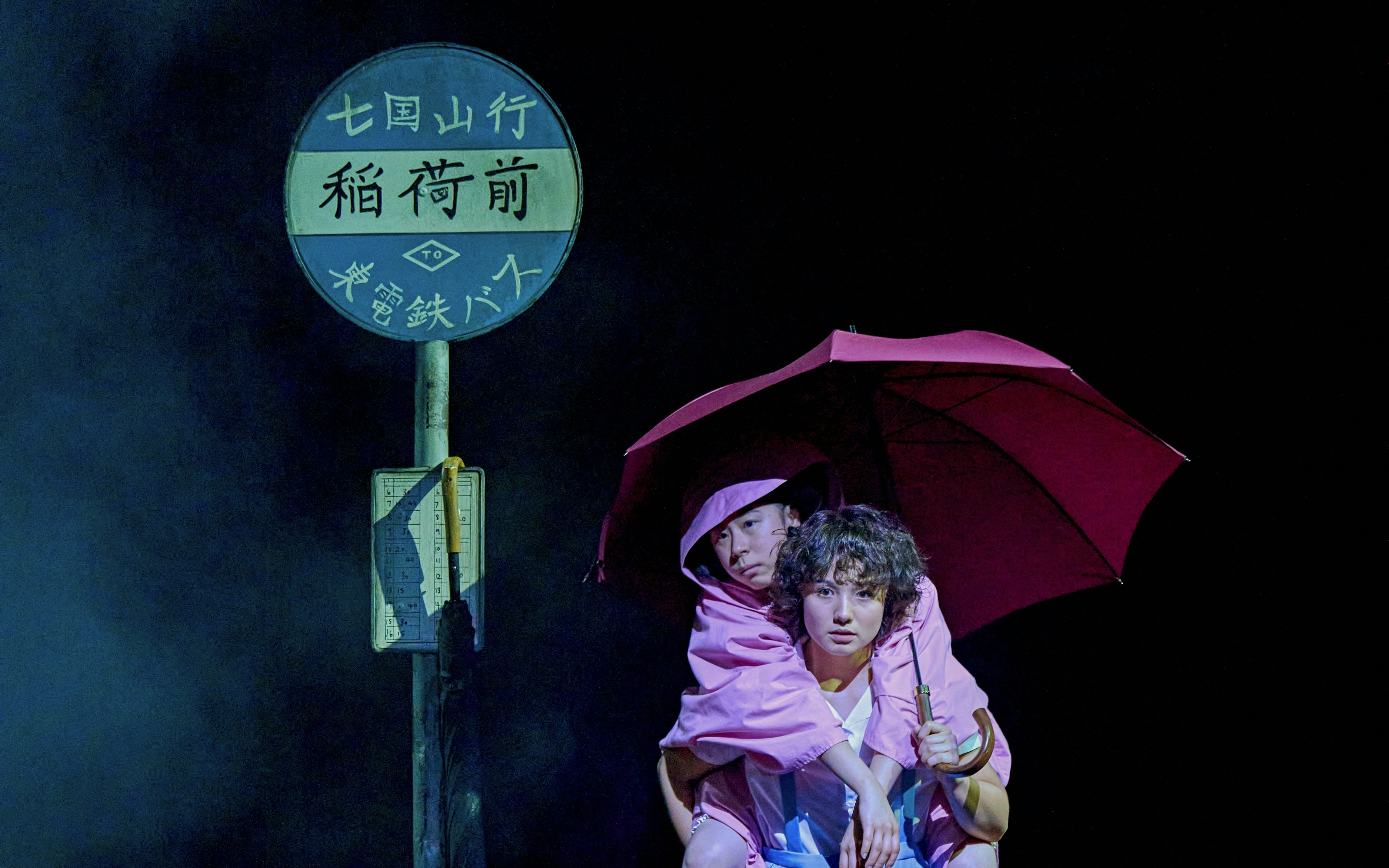 Two people in pink raincoats under an umbrella at a bus stop, My Neighbour Totoro production.