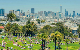 People relaxing in Dolores Park with San Francisco skyline in the background.