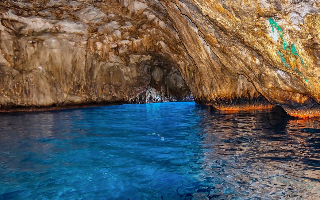 Blue waters inside Grotta Azzurra cave, Capri, with rocky walls reflecting light.