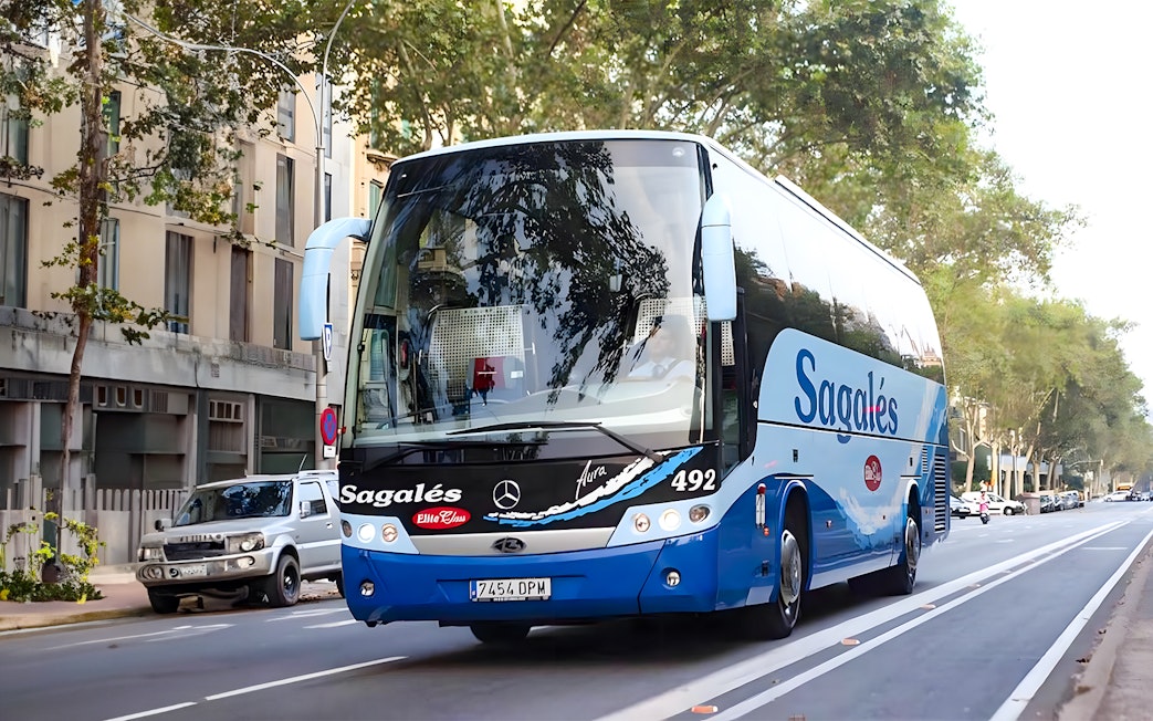 Bus for Girona Airport transfer to Barcelona city center on a tree-lined street.