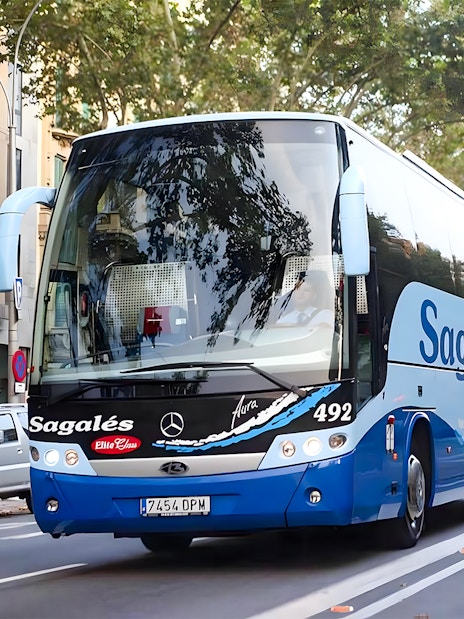 Bus for Girona Airport transfer to Barcelona city center on a tree-lined street.