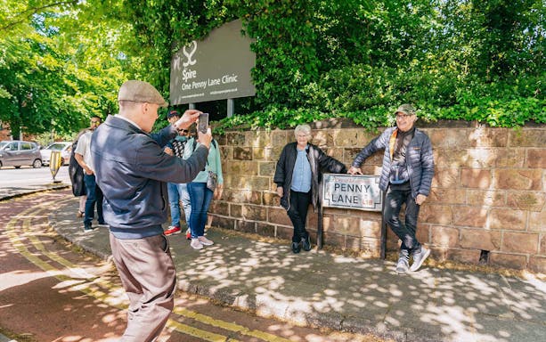 Guide photographing couple at Penny Lane sign, Liverpool.