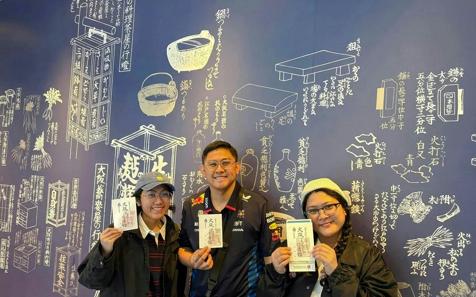 Tourists holding tickets at Osaka Castle bike tour with Japanese mural background.