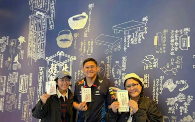 Tourists holding tickets at Osaka Castle bike tour with Japanese mural background.
