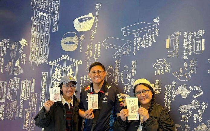 Tourists holding tickets at Osaka Castle bike tour with Japanese mural background.
