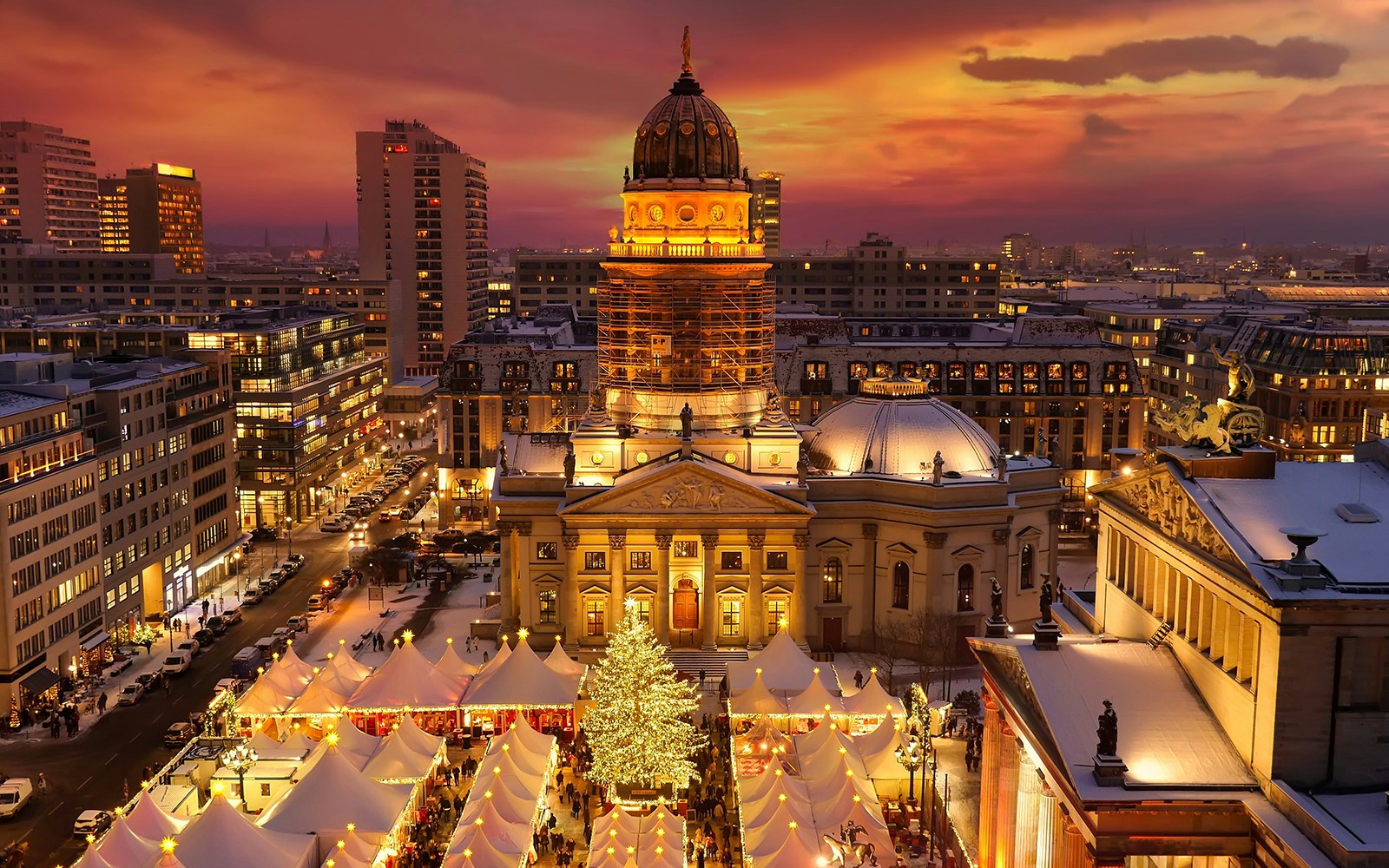 Weihnachtsmarkt am Gendarmenmarkt in Berlin bei Sonnenuntergang, mit einem geschmückten Baum und beleuchteten Ständen.