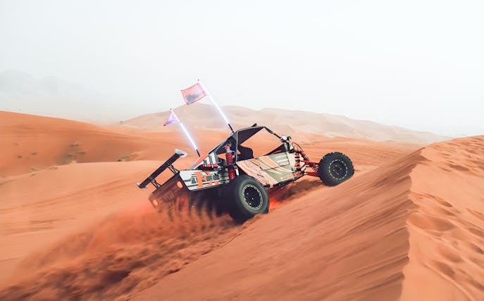 Dune buggy driving over sand dunes in Dubai desert.