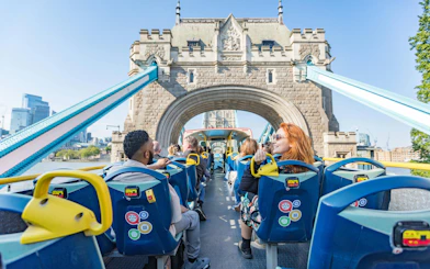 Passengers on an open-top bus crossing Tower Bridge, London, during a hop-on hop-off tour.