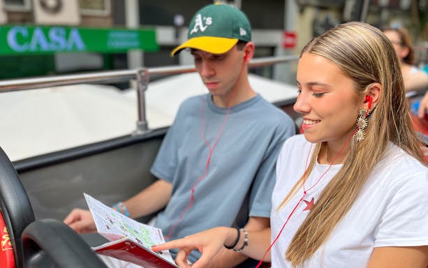 Tourists with earphones studying a city map on a double-decker bus.