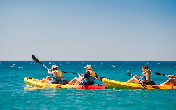 Kayakers paddling in clear waters of Arrábida Natural Park, Lisbon, with rocky cliffs in the background.