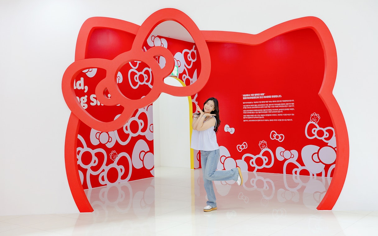 Tourist posing under red Hello Kitty arch at Hello Kitty Island.