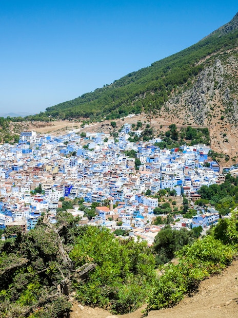 Traveler capturing panoramic view of Chefchaouen, Morocco, with blue buildings on Rif mountain slopes.