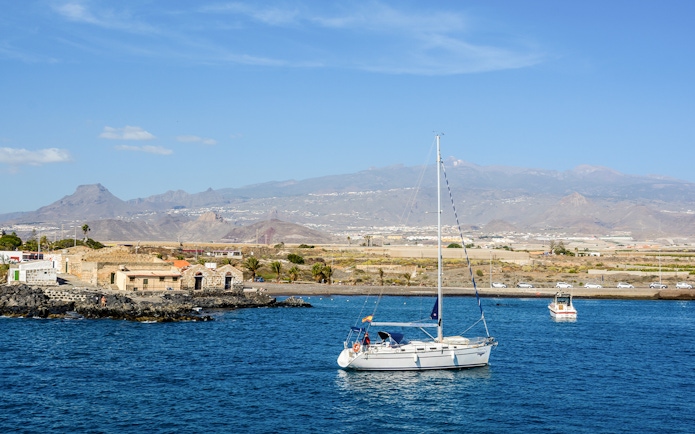Sailboat on the water near Marina del Sur, Las Galletas, Tenerife, Spain with mountains in the background.