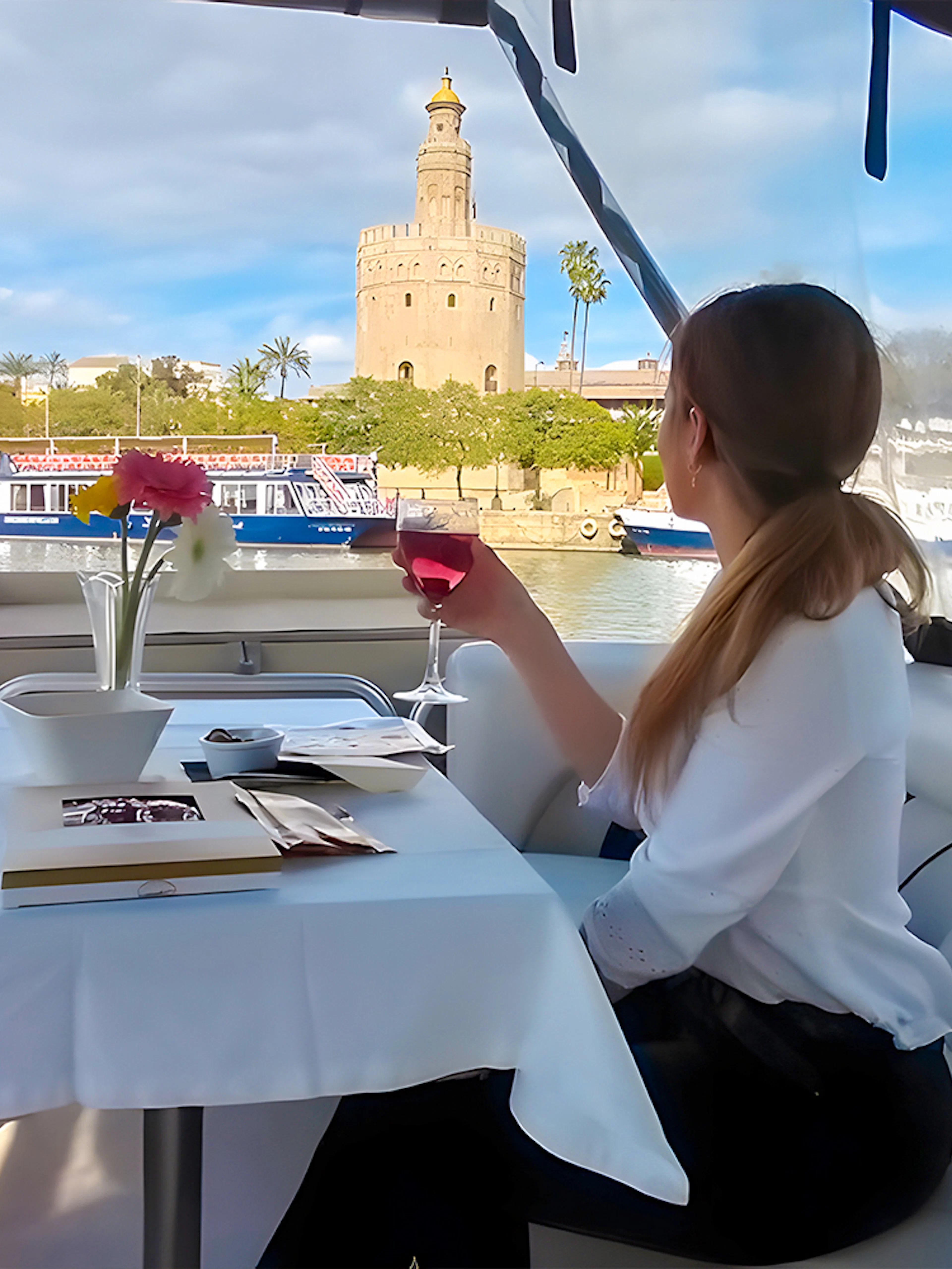 Tourist on Guadalquivir River Cruise enjoying view of Torre del Oro with tapas and drink.